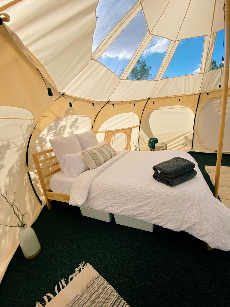 A furnished glamping tent with beds and warm interior lighting.