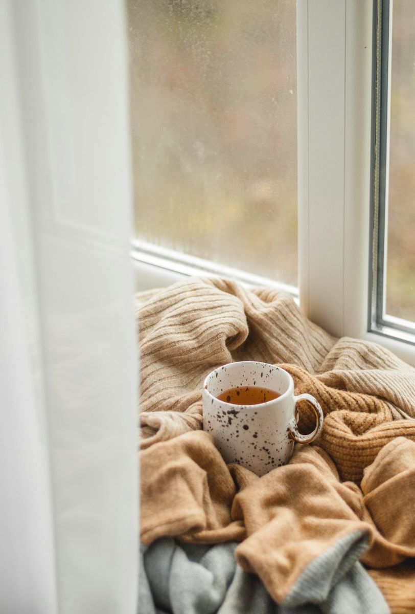 Speckled mug of tea on a knitted blanket beside a window