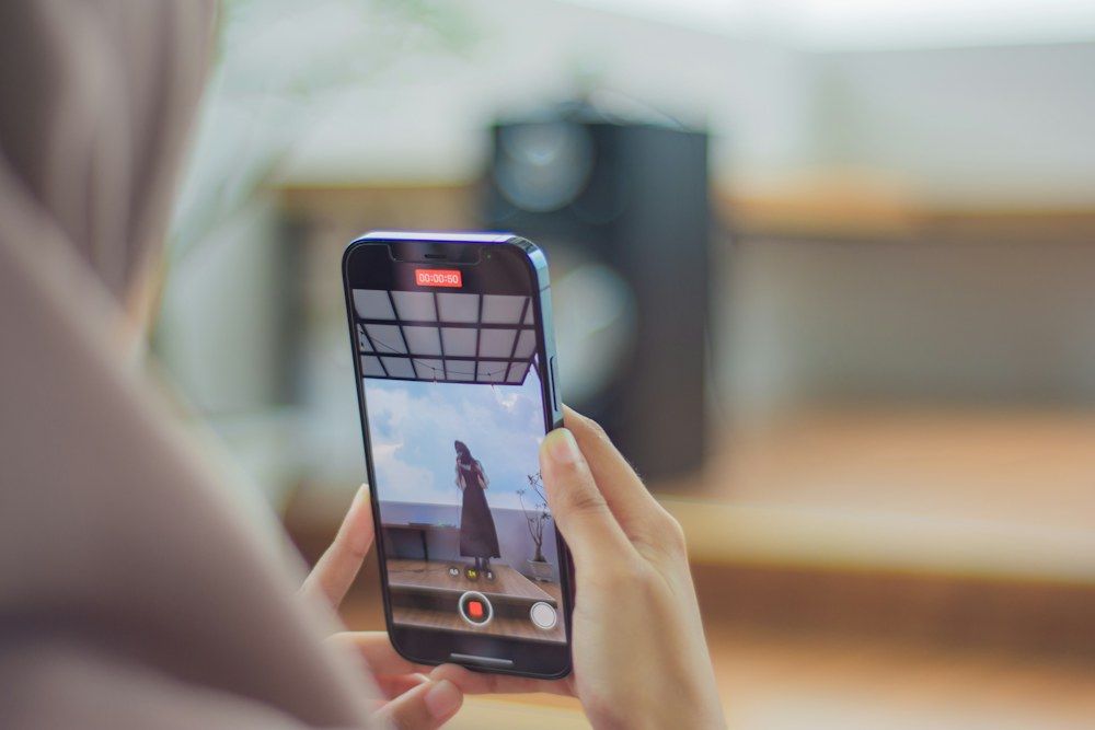 A pair of hands holds a smartphone in landscape orientation, actively recording a woman dancing on a rooftop terrace.