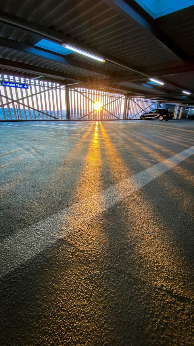 A lone black car is parked on the top level of a multi-story garage just as the sun dips below the horizon.