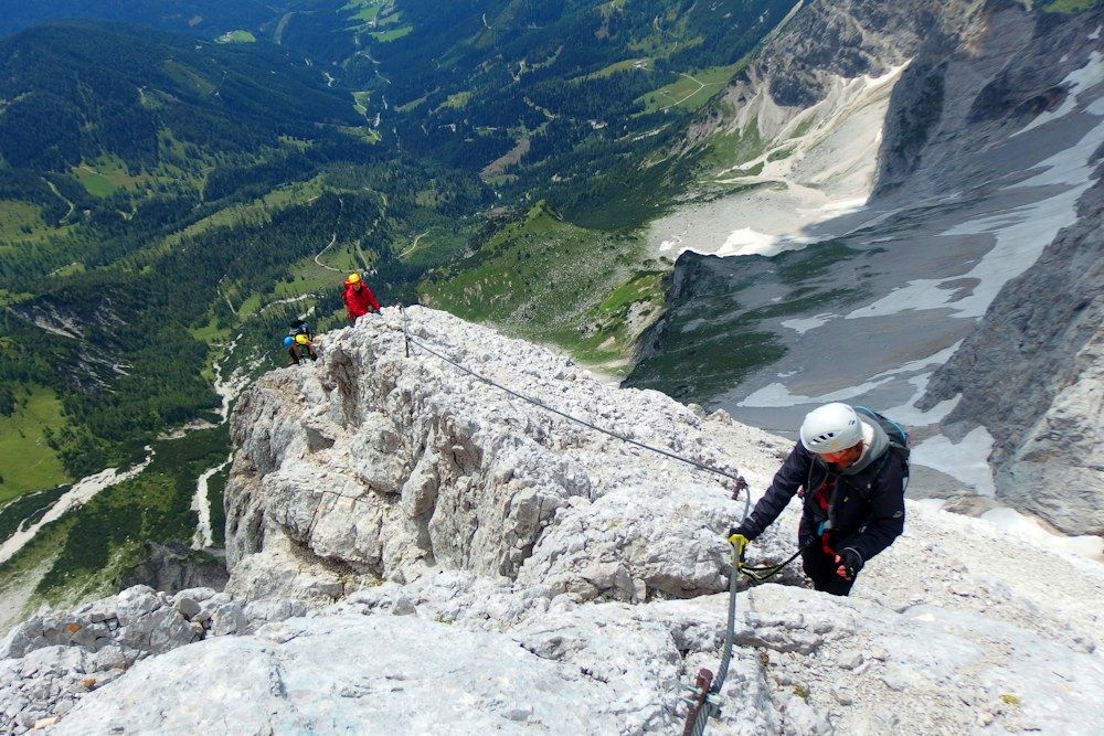 Helmeted climbers following a fixed cable along an alpine ridge